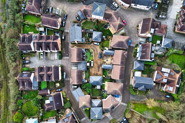 Aerial view of a residential neighborhood showcasing circular arrangement of houses, driveways, and parked cars, surrounded by greenery and trees - property photography by Ben