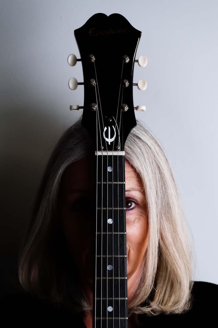 A woman with blonde hair is holding an acoustic guitar.