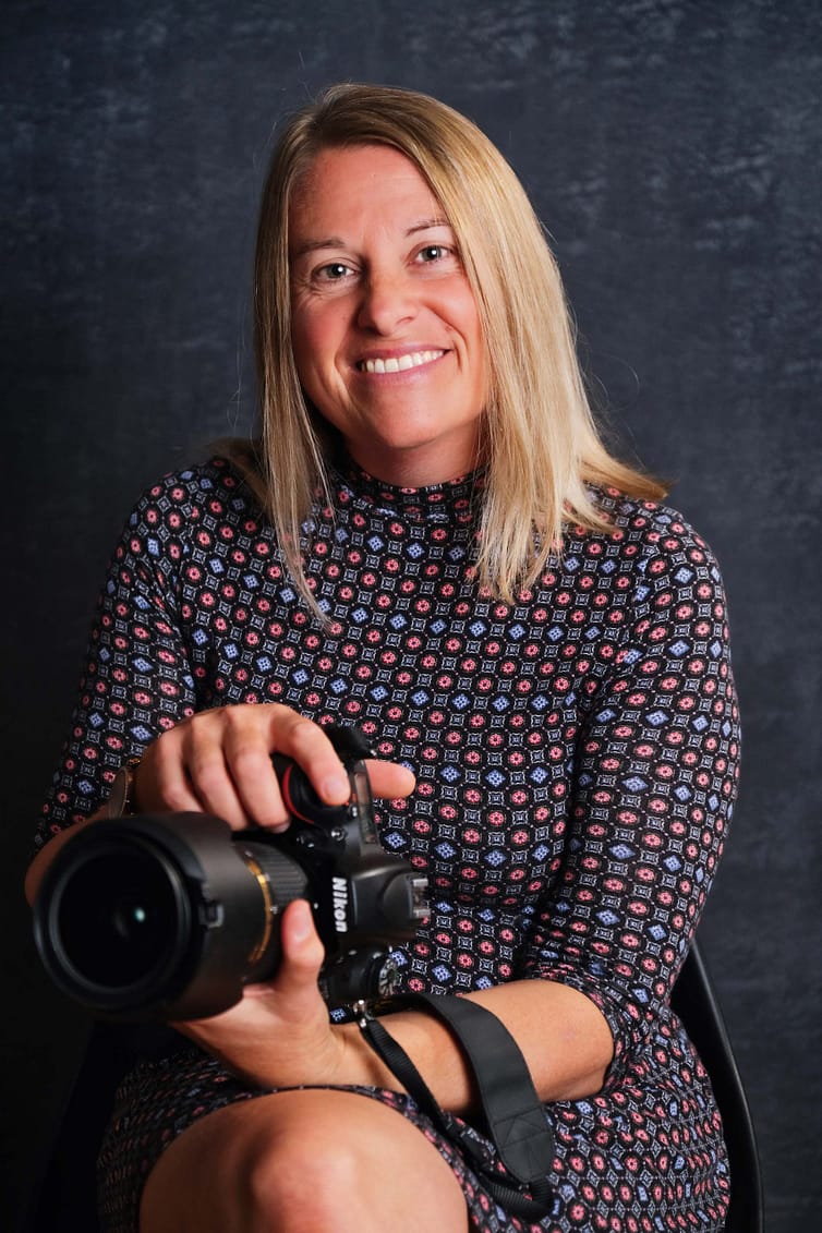A woman holding a camera in front of a black background.