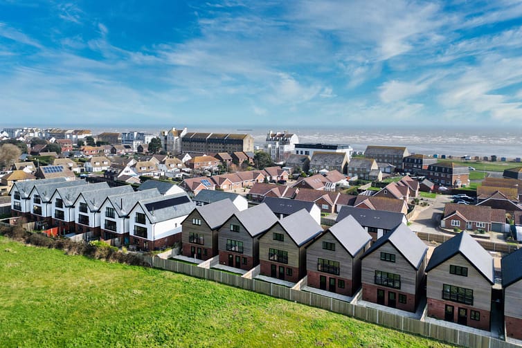 Aerial view showcasing a residential area with uniform modern houses, traditional homes, and green fields under a partly cloudy sky - aerial property photography by Ben
